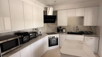 Een moderne keuken met witte kastjes, een ingebouwde oven, een magnetron en een koffiezetapparaat.