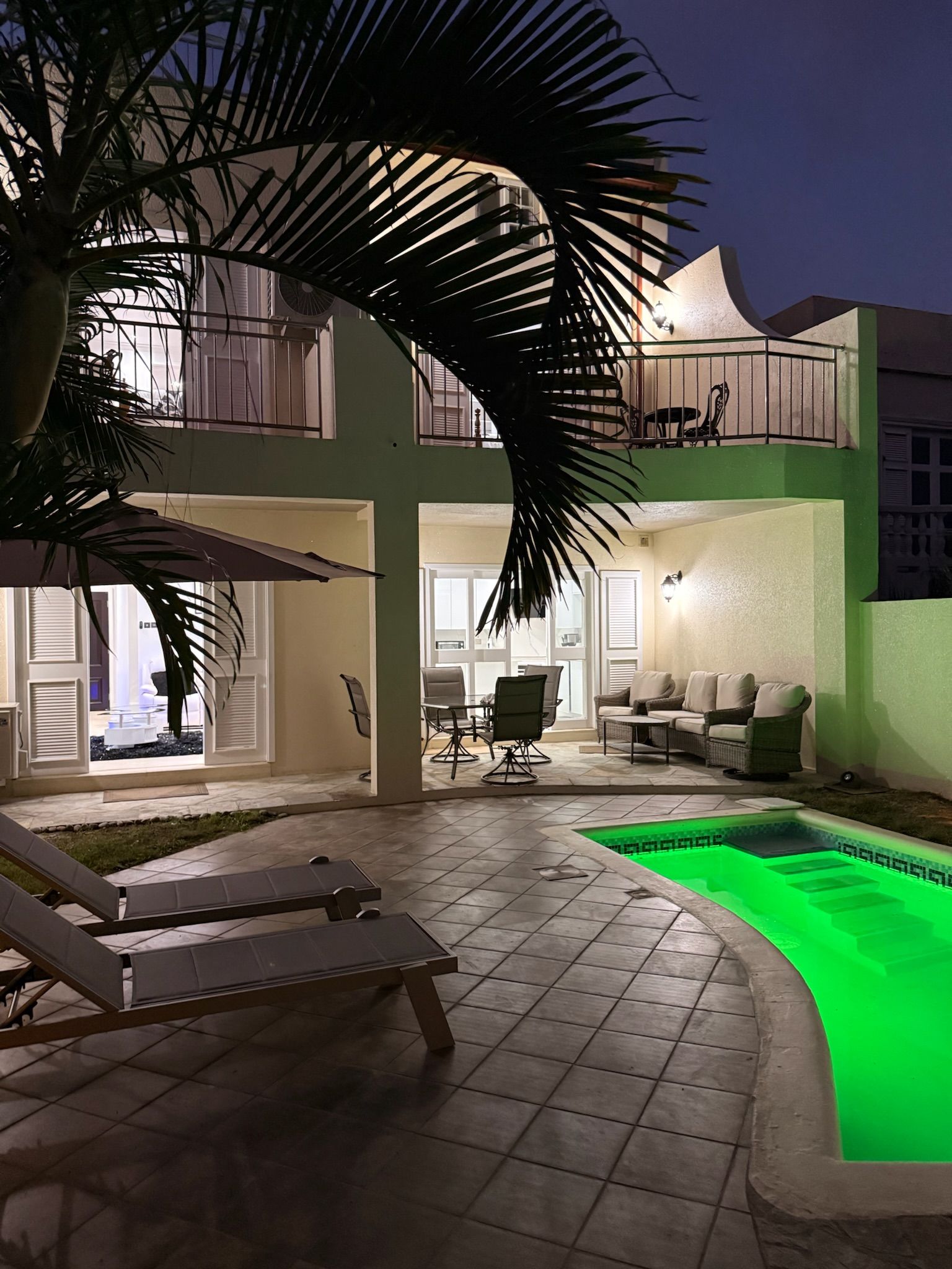 Ein zweigeschossiges Gebäude mit Swimmingpool, Außenbereich und einer Palme.