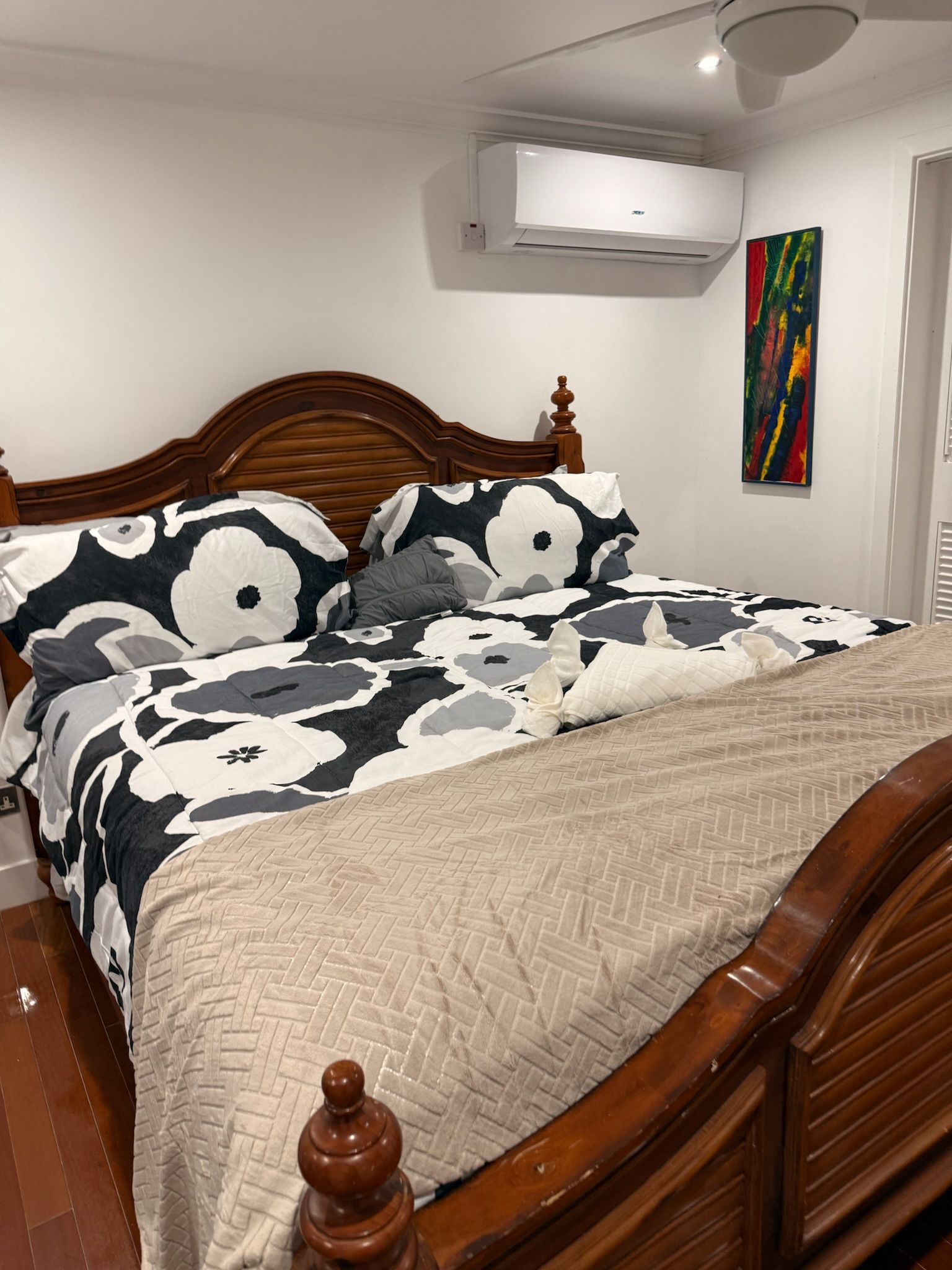 Un dormitorio con una cama de madera, una colcha estampada, un edredón color crema y un equipo de aire acondicionado en la pared.