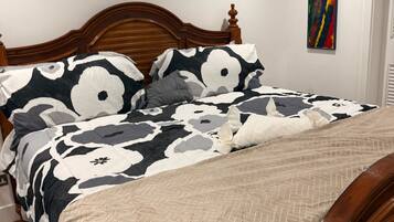 Un dormitorio con una cama de madera, una colcha estampada, un edredón color crema y un equipo de aire acondicionado en la pared.
