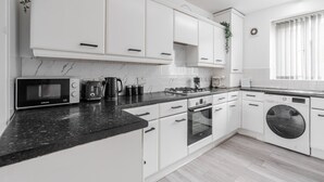 A modern kitchen with white cabinets, a black countertop, a microwave, a toaster, a kettle, a stove, an oven, and a washing machine.