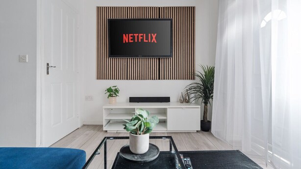 A modern living room with a mounted TV displaying 'NETFLIX', a white entertainment unit, a coffee table with a plant, and a blue sofa.