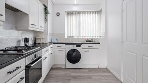 A compact kitchen with white cabinets, a black stove, a washing machine, and a window with blinds.