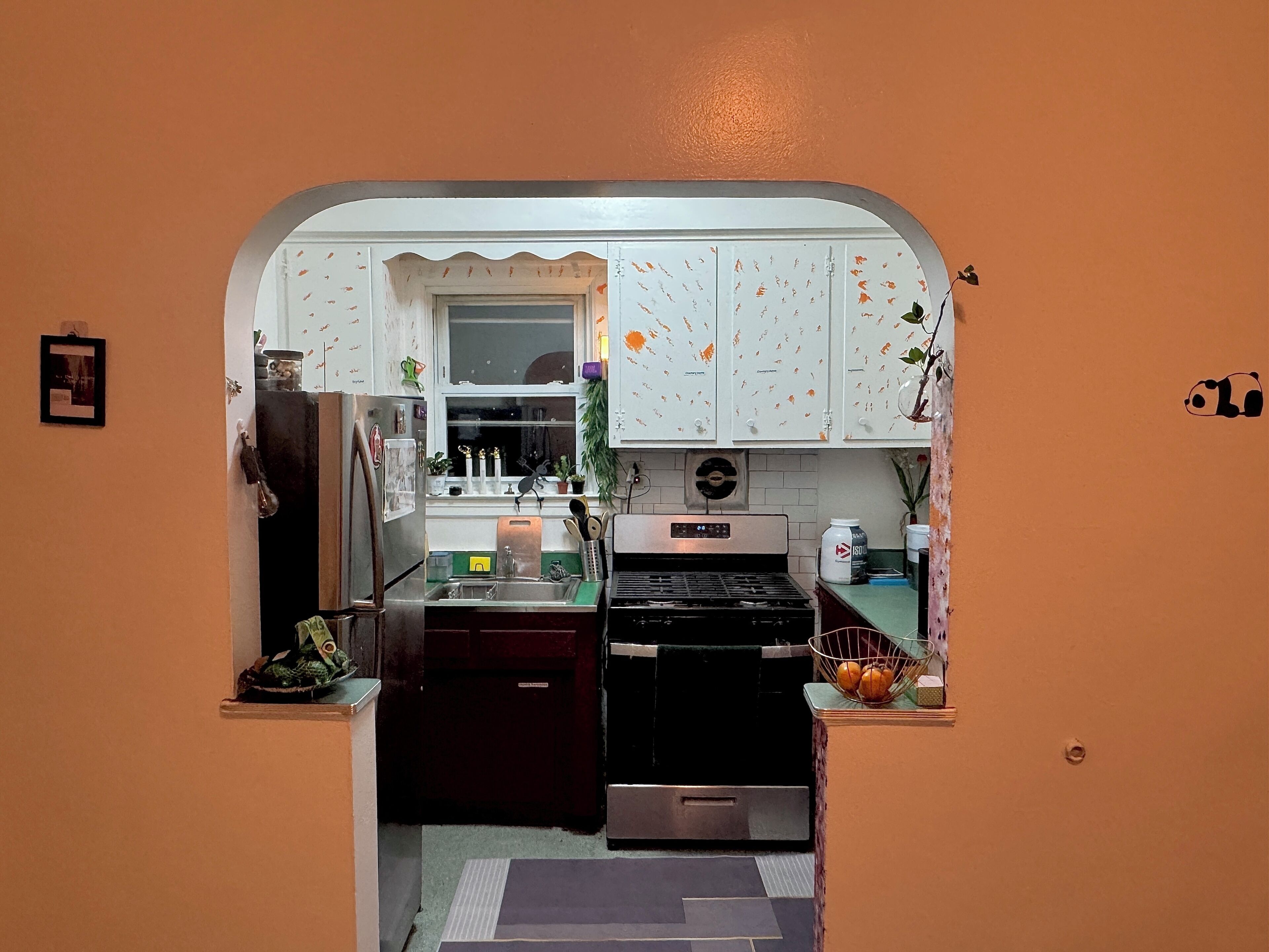 A compact kitchen with white cabinets, a stainless steel refrigerator, a black stove, and a sink.