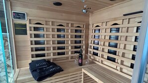 Ein Saunaraum mit Holzbänken, einer Bank mit Handtuch, einer Flasche und Weingläsern.