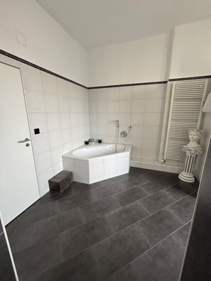Une salle de bain moderne avec une baignoire sur pieds, des murs recouverts de carreaux blancs et un sol carrel é de couleur foncée.
