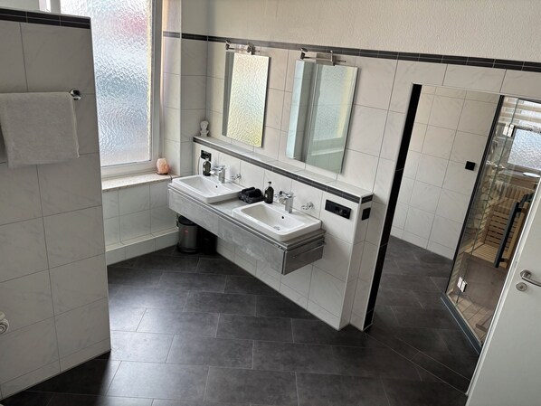 Une salle de bain moderne avec deux lavabos, un grand miroir et une douche à l’italienne.