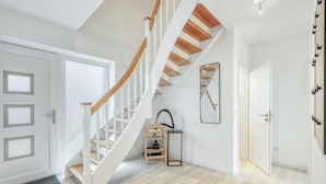 Un interior moderno con una escalera de madera, un espejo y un pequeño estante con objetos.