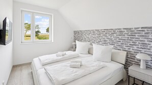 A bedroom with a sloped ceiling, a large window with a view of a field, a brick-patterned headboard, and a bedside table with a lamp.