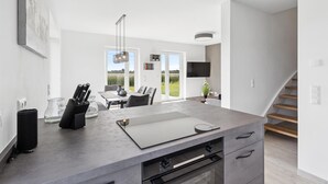 A modern kitchen with a large island, a dining area with a view, and a staircase.