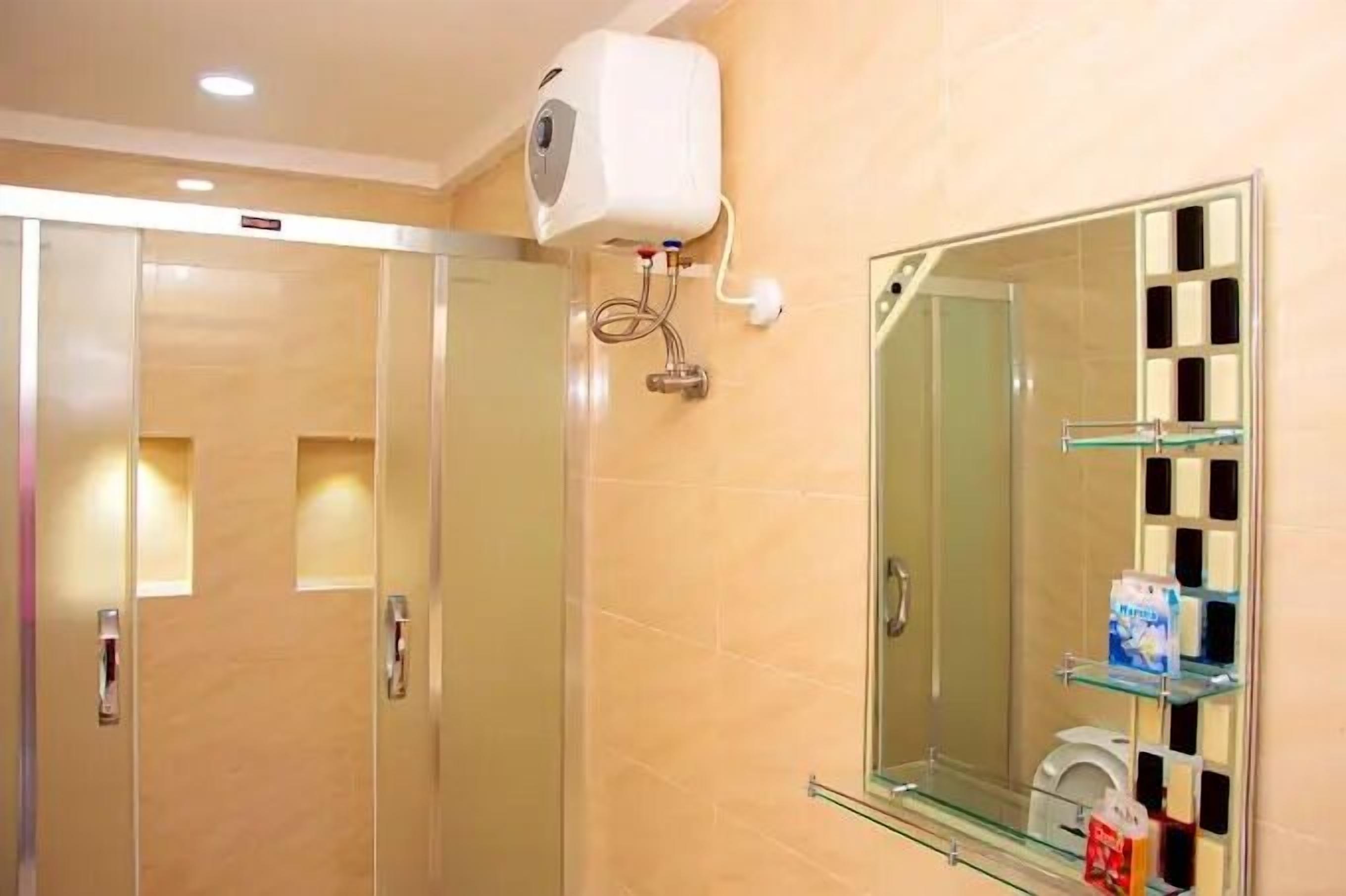 A bathroom with a glass shower enclosure, a wall-mounted air conditioning unit, and a glass shelf with toiletries.