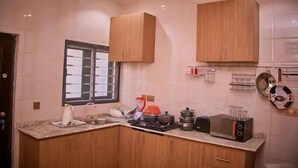 A modern kitchen with wooden cabinets, a window, and various appliances including a kettle, pots, and a toaster. - Ramlat Apartment  (Kano)