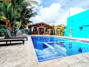 A swimming pool with a wooden deck, lounge chairs, and a building with a porch. - Style and Comfort: Tropical Studio Cabina A/C Pool (Herradura)