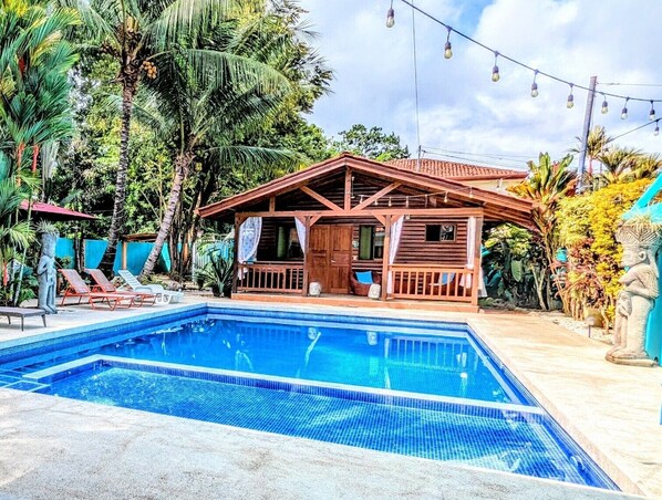 A wooden house with a pool, surrounded by tropical vegetation and a string of lights. - Style and Comfort: Tropical Studio Cabina A/C Pool (Herradura)