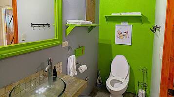 A bathroom with a glass sink, a white toilet, and green walls.