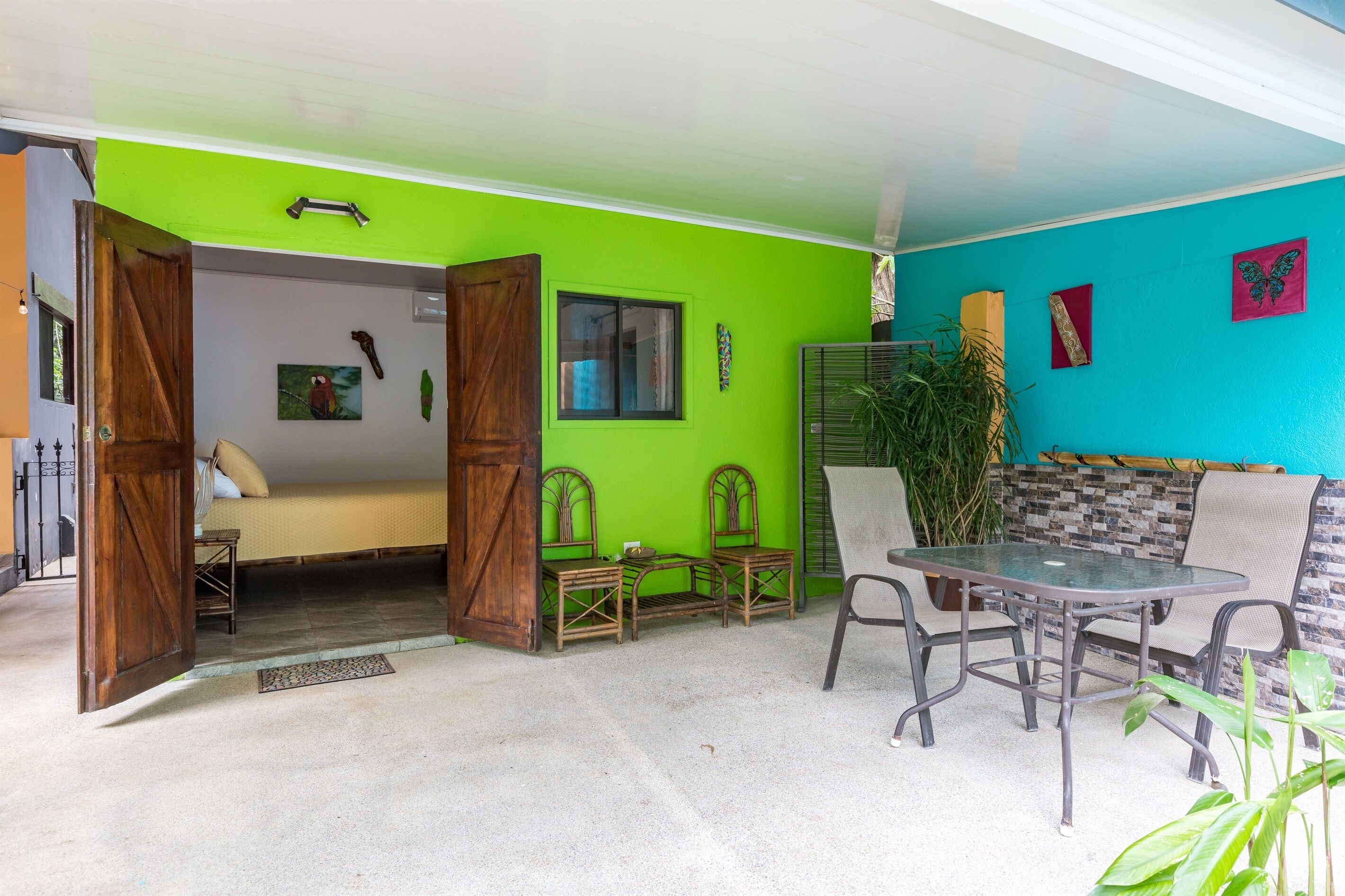 A room with a green wall, a bed, a table with chairs, and a window.