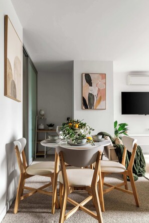 Un comedor con una mesa redonda, cuatro sillas de madera, un jarrón con flores y un televisor de pantalla plana montado en la pared.