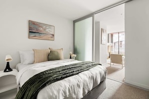 Un dormitorio moderno con una cama grande, un cuadro y un ventanal corredera que da a un balcón.