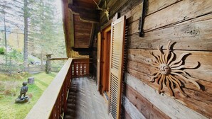 A wooden cabin with a balcony, a wooden wall with a sun design, and a small statue in the yard. - Idyllic Cabin With Sauna (Bad Kleinkirchheim)