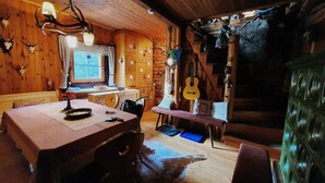 A rustic cabin interior with wooden walls, a dining table, chairs, a window, and a guitar hanging on the wall. - Idyllic Cabin With Sauna (Bad Kleinkirchheim)