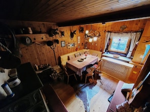 Ein gemütliches Blockhaus-Interieur mit einem Holzespeisetisch, Stühlen, einer kleinen Küchenzeile und einem Fenster mit Vorhängen.