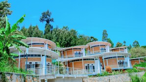 A multi-story building with curved balconies, surrounded by greenery and trees. - Kivu Breeze Hotel (Bwishyura)