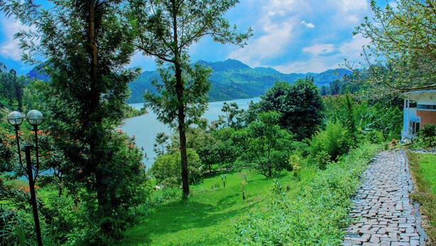 A stone pathway leading to a house with a view of a lake and mountains. - Kivu Breeze Hotel (Bwishyura)