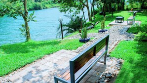 A bench by a river with a stone pathway and potted plants. - Kivu Breeze Hotel (Bwishyura)