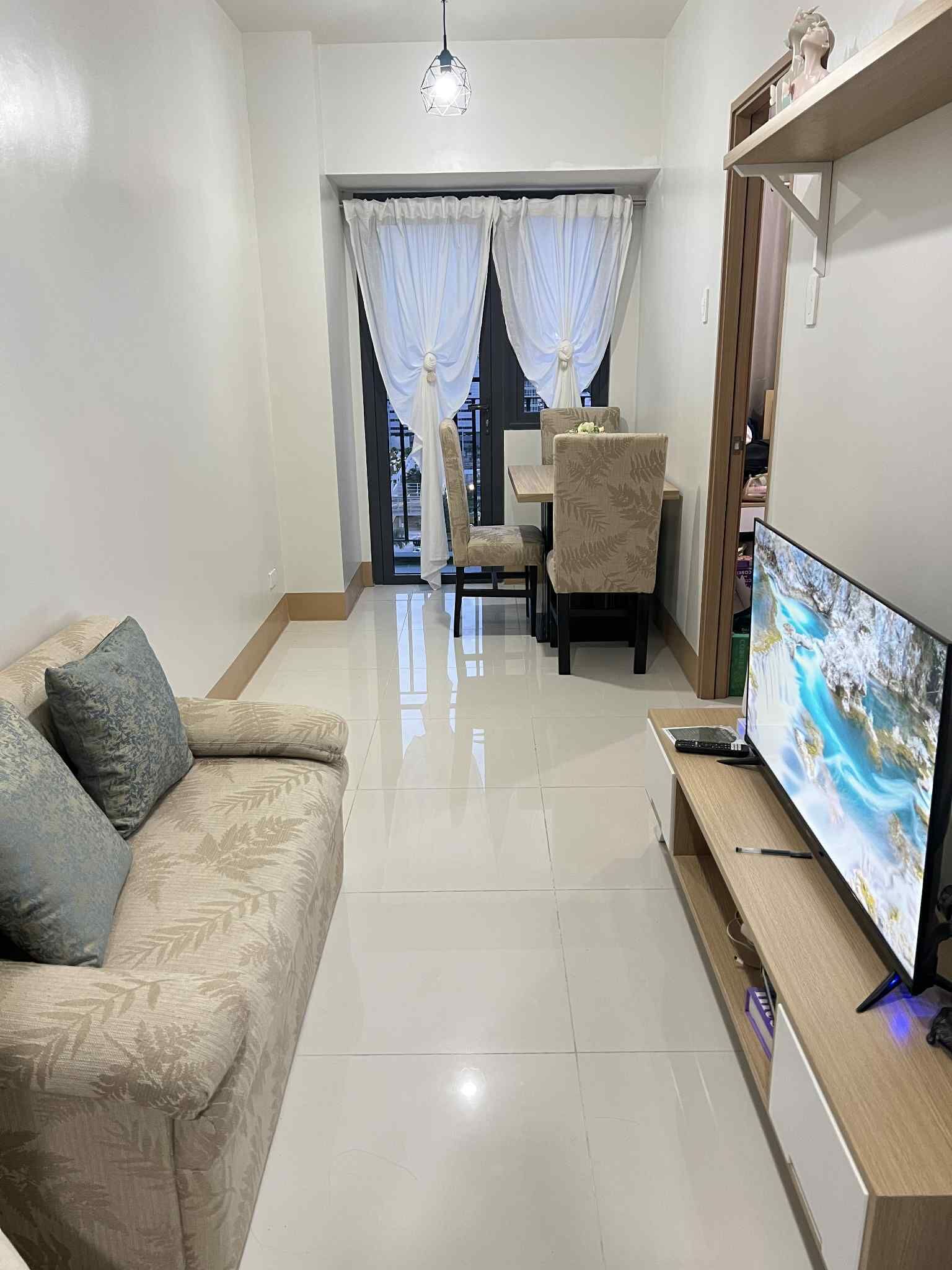 Un salon comprenant un canapé, un téléviseur, un coin repas avec une table et des chaises, et une fenêtre avec des rideaux.