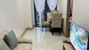 A living room with a sofa, a TV, a dining area with a table and chairs, and a window with curtains. - CONDO NEXT DOOR PH (Pasay)
