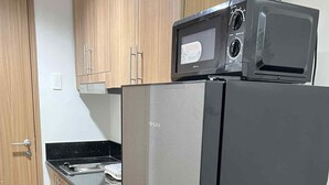 A kitchen with wooden cabinets, a black refrigerator, and a microwave on top. - CONDO NEXT DOOR PH (Pasay)
