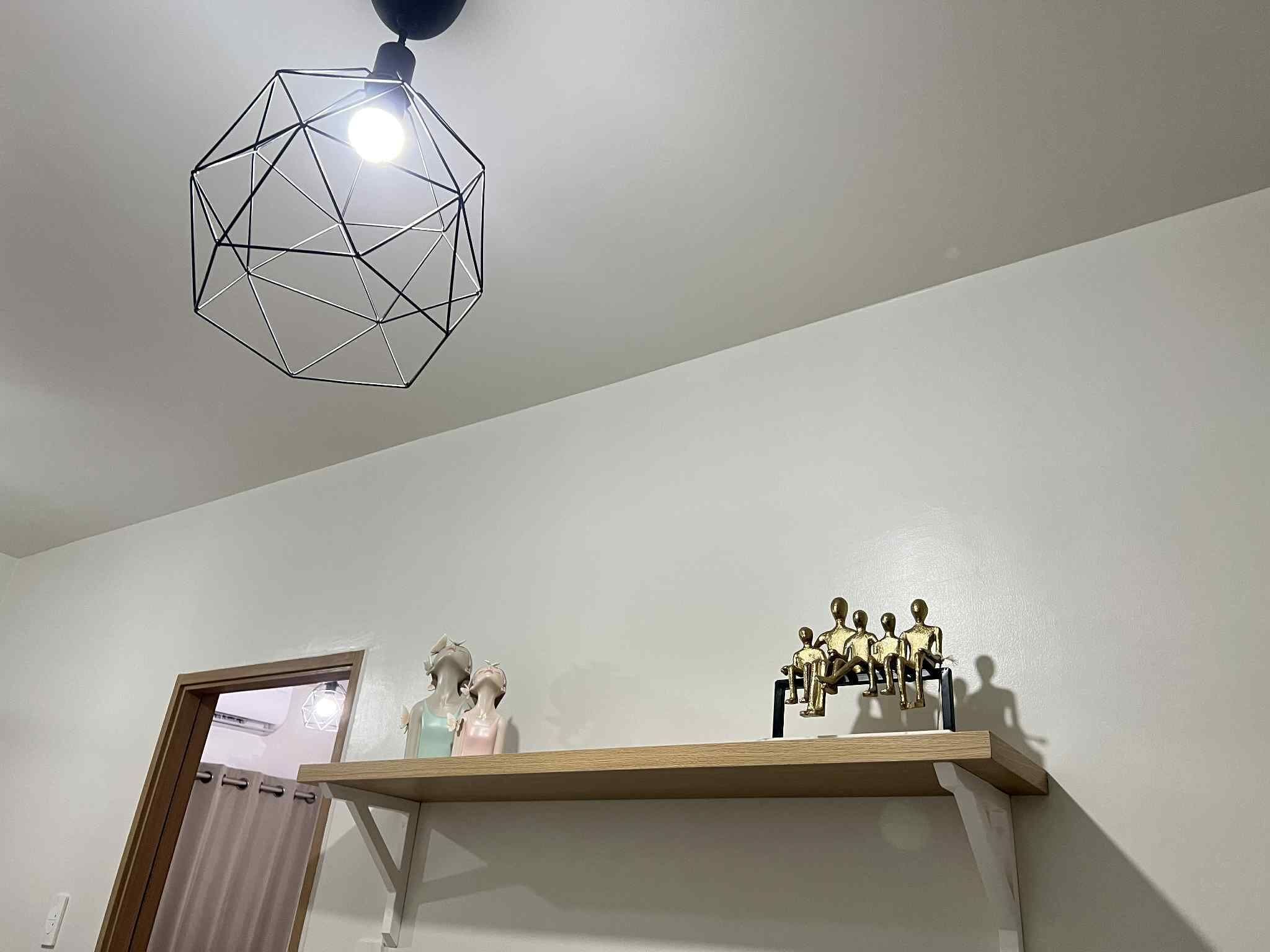 Una habitación con una lámpara colgante de diseño geométrico, un estante de madera con figuritas, y una puerta con cortina.