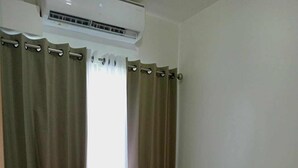 A neatly made bed with white linens in a room with a wooden headboard and a window with curtains. - CONDO NEXT DOOR PH (Pasay)