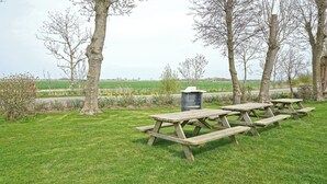 A picnic area with wooden tables and benches, surrounded by trees and a grassy field.