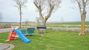 A playground with a slide and a mailbox in a grassy area with trees and fields.