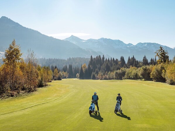 A golf course with two players, a clear sky, and mountains in the background.