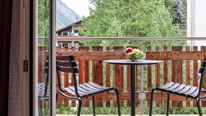 Ein Balkon mit Holzzaun, zwei Metallstühlen, einem kleinen runden Tisch mit Obstschale und Blick auf die Berge.