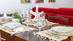 A dining table set with plates, glasses, and a pitcher, with a red couch in the background. - Beautiful private villa for 4 people with TV and terrace (Badesi)