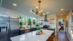 Une cuisine moderne dotée d’un grand îlot central, d’appareils électroménagers en acier inoxydable et d’un lustre original.