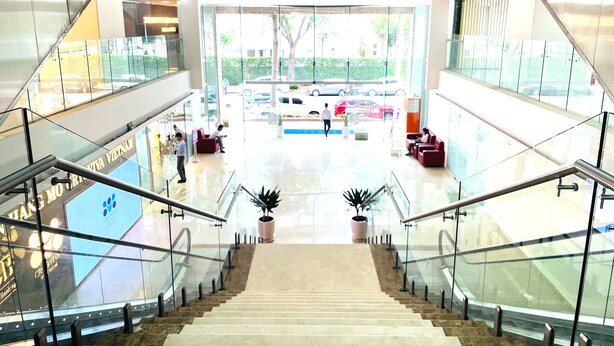 Un espacio interior moderno con una escalera central, barandillas de vidrio y vistas al exterior a través de amplios ventanales.