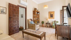 Un salon avec une porte en bois, un canapé, une table basse, une bibliothèque, une lampe et un téléviseur.