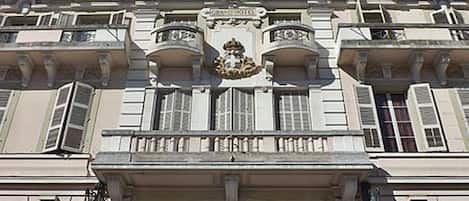 A classical building with ornate balconies, a central entrance with a decorative arch, and a crest above the entrance.