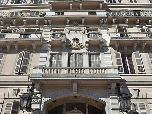 A classical building with ornate balconies, a central entrance with a decorative arch, and a crest above the entrance.