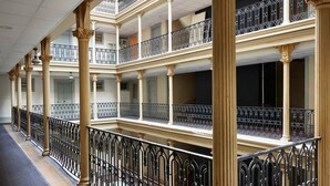 Corridoio di un hotel su più piani, con ringhiere nere decorate e colonne in stile classico.