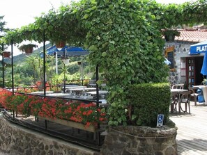 An outdoor dining area with a stone wall, a pergola covered with green vines, and a sign indicating wheelchair accessibility. - Chalet with Terrace and Garden Furniture in Darbres (Darbres)