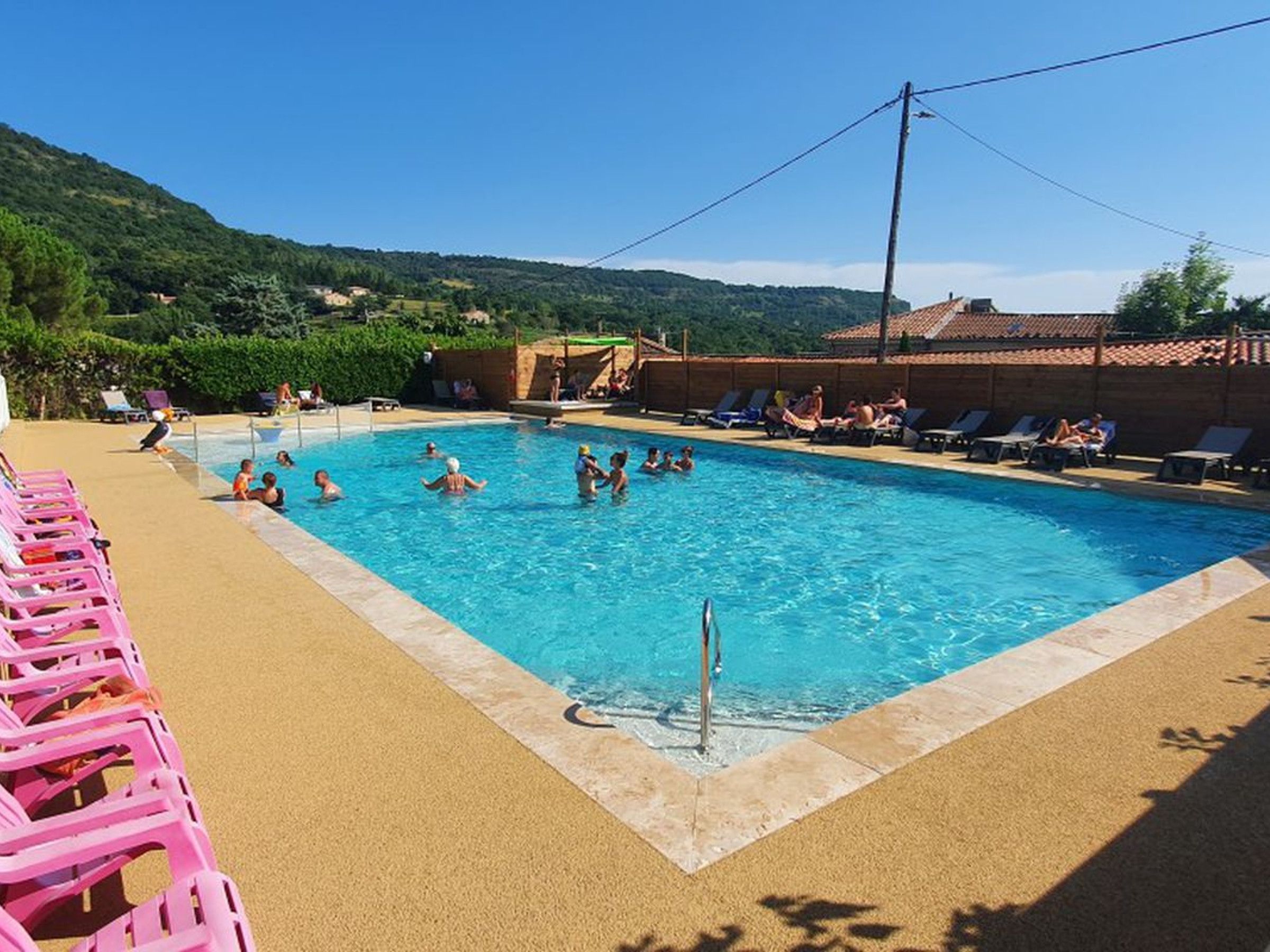 Une piscine où l’on voit des personnes dans l’eau, entourée de chaises longues et d’une zone sablonneuse.