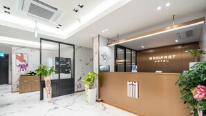 Eine moderne Hotelrezeption mit Marmorboden, einer Rezeption und Topfpflanzen.