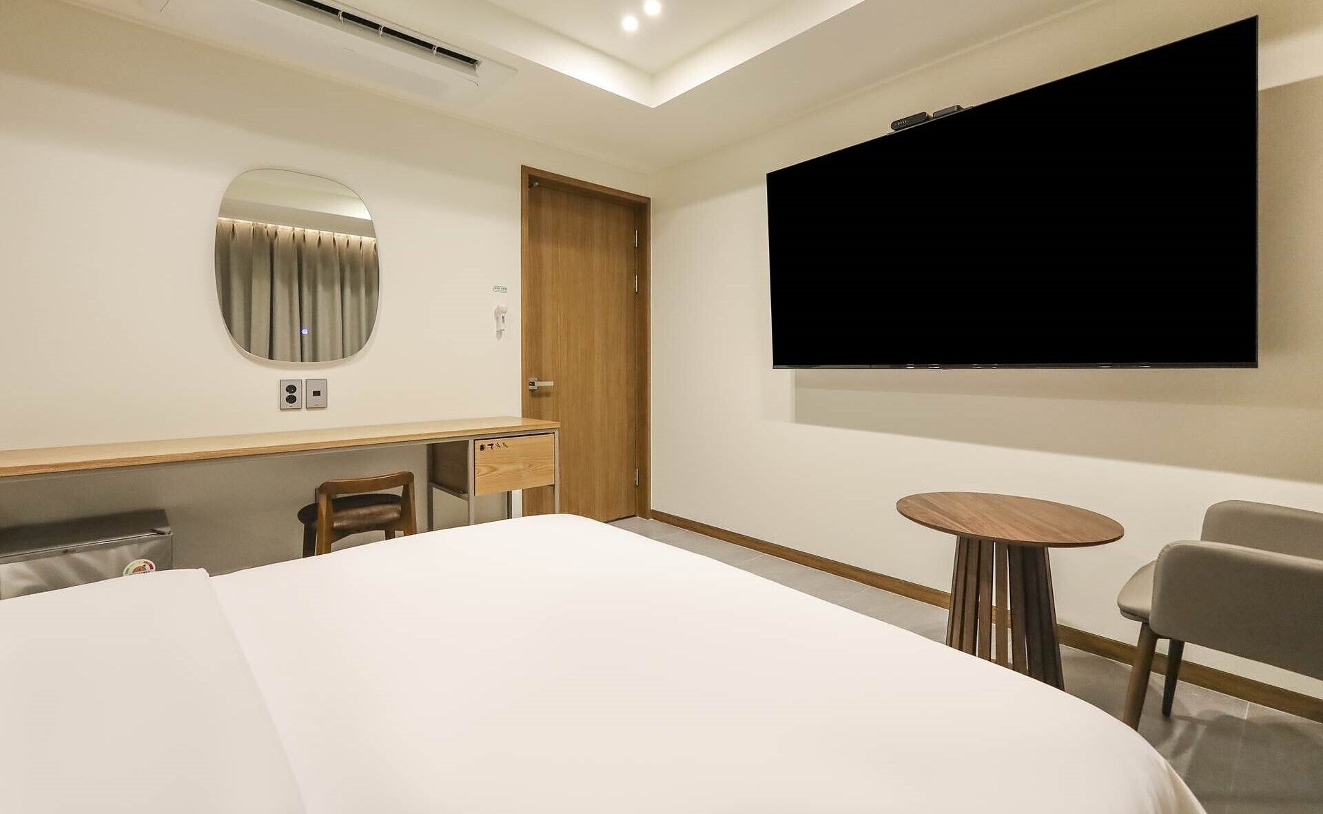 Ett hotellrum med en säng, ett skrivbord med en stol, en tv och ett litet bord.