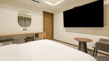Habitación de hotel con cama, escritorio con silla, televisor y una mesita.