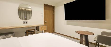 A hotel room with a bed, a desk with a chair, a TV, and a small table.
